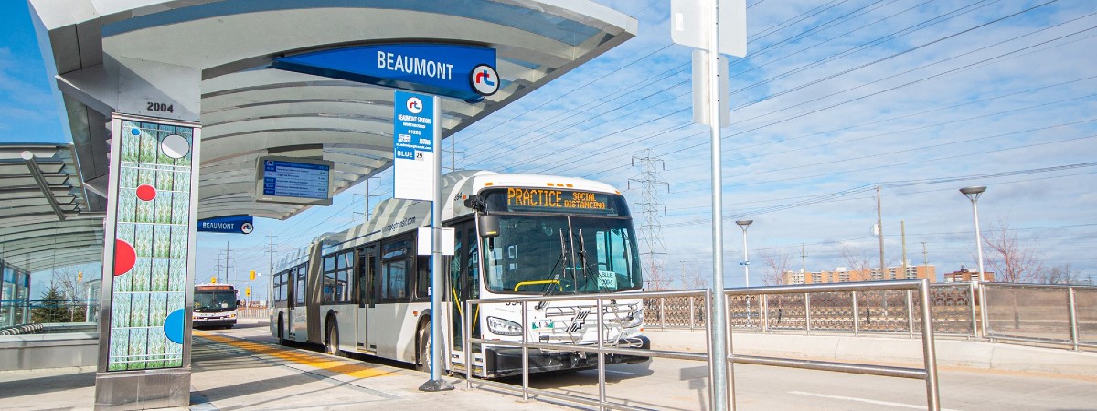 A bus stopped at Beaumont Station displays text in a digital sign that reads PRACTICE SOCIAL DISTANCING