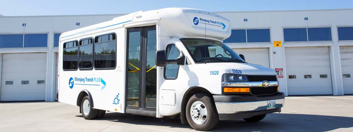 A Winnipeg Transit Plus vehicle, marked with a logo, parked in front of the Winnipeg Transit garage